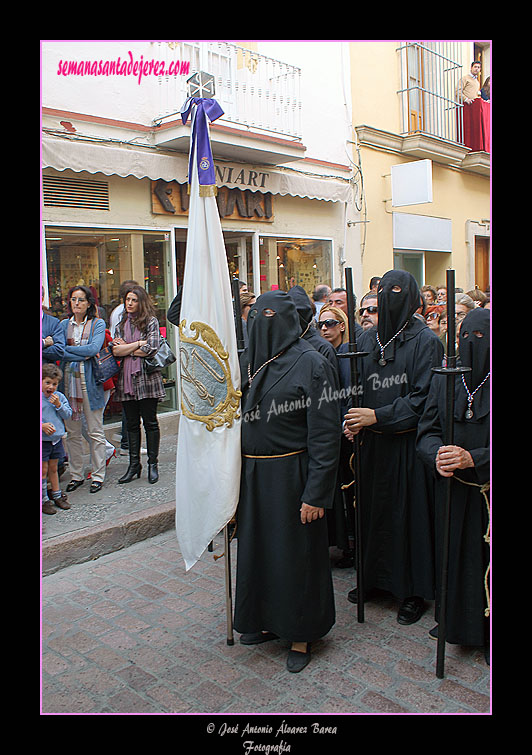 Nazareno portando la Bandera de Devotos de la Hermandad de Nuestra Señora de Amor y Sacrificio