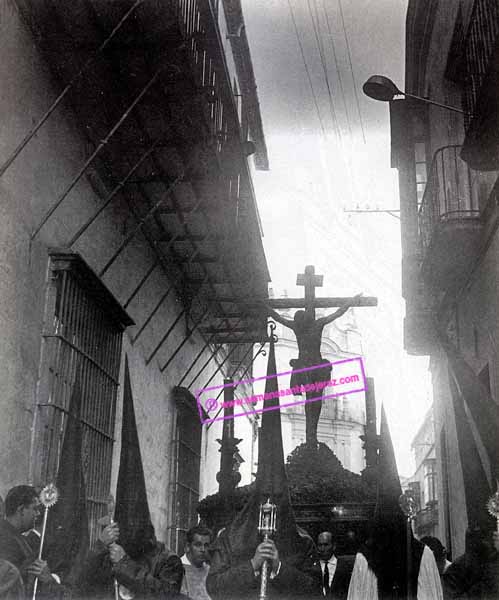 Bello contraluz del paso de misterio de la Hermandad de la Buena Muerte. En primer plano los tornapuntas del palacio de los marqueses de los Alamos del Guadalete. (Foto: Eduardo Pereiras, año 1964)