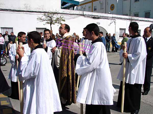 Preste acompañado de acólitos detras del paso de María Santísima del Consuelo